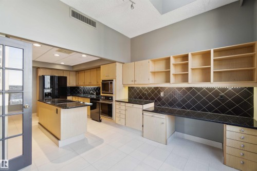 Kitchen featuring an island, black appliances, light wood-finish cabinetry, black countertops, and a black patterned backsplash - #12A 10050 118 St Nw, Edmonton, AB 
