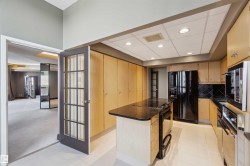 Kitchen featuring wood-finish cabinetry, black appliances, a black countertop island, and tile flooring - 