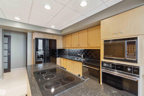Kitchen featuring light wood cabinetry, black tile backsplash, built-in microwave, integrated wall oven, and a center island with an electric cooktop - #12A 10050 118 St Nw, Edmonton, AB 