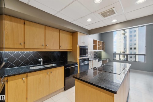 Kitchen featuring recessed lighting, a built-in microwave, wood-finish cabinetry, a double basin sink, and an island with a cooktop - #12A 10050 118 St Nw, Edmonton, AB 