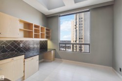Built-in cabinetry with light wood finish and polished hardware, black patterned backsplash, dark stone-finish countertop, and large window - 