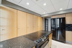Kitchen featuring an integrated cooktop, dark speckled countertops, black stainless steel refrigerator, and extensive light wood-finish cabinetry - 