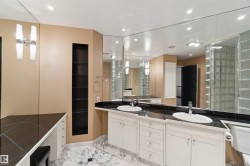 Dual vanities with undermount sinks and black countertops, extensive wall-mounted mirrors, recessed lighting, and a glass block shower enclosure - 
