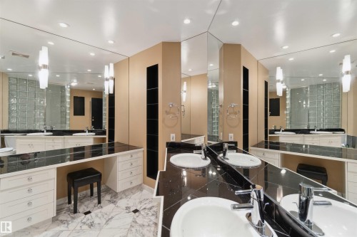 Dual vanity with undermount sinks, chrome fixtures, dark stone countertops, extensive wall-mounted mirrors, and glass block architectural feature - #12A 10050 118 St Nw, Edmonton, AB 