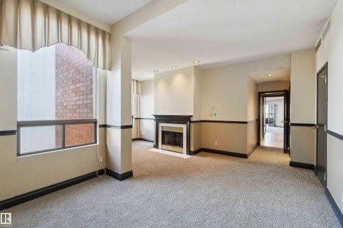 Recessed lighting, a fireplace with a black mantel and white surround, and light-toned carpet flooring - #12A 10050 118 St Nw, Edmonton, AB 