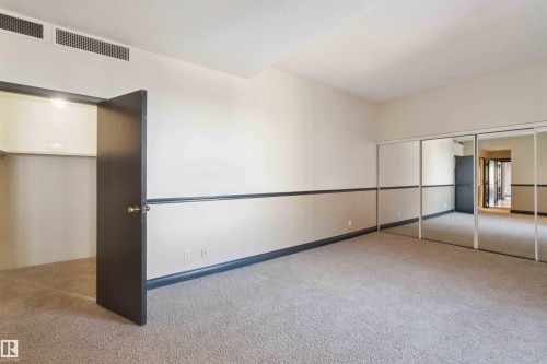 Spacious room featuring carpeting, mirrored closet doors, a built-in closet with shelving, and a chair rail - #12A 10050 118 St Nw, Edmonton, AB 