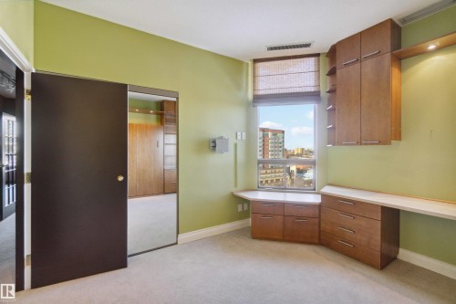 Built-in desk with extensive cabinetry, large window with roller shades, and light-toned carpeting - #12A 10050 118 St Nw, Edmonton, AB 
