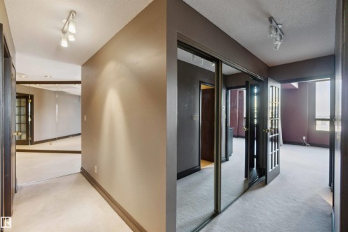 Textured ceiling with track lighting, mirrored closet doors, paneled interior doors, and neutral carpeting - #12A 10050 118 St Nw, Edmonton, AB 