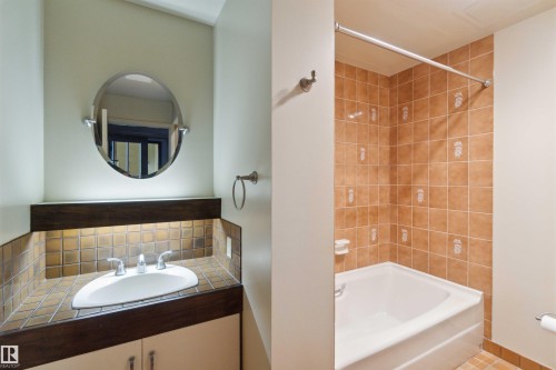 Bathroom featuring a tiled shower and tub combination, a built-in vanity with under-cabinet storage, a white oval sink, and a framed oval mirror - #12A 10050 118 St Nw, Edmonton, AB 