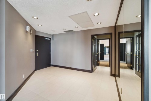 Recessed ceiling lighting, light-toned tile flooring, mirror-paneled wall, dark wood trim, and multiple doorways - #12A 10050 118 St Nw, Edmonton, AB 