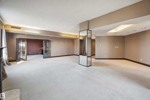 Expansive carpeted area with recessed lighting, mirrored architectural column, and French doors leading to an adjacent room - #12A 10050 118 St Nw, Edmonton, AB 
