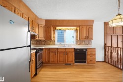 Kitchen featuring wood cabinetry, light-toned countertops, a stainless steel refrigerator, a black dishwasher, and wood-finish flooring - 
