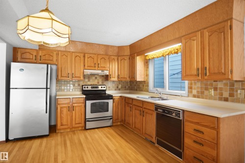 Kitchen featuring wood cabinetry, light-toned countertops, a stainless steel refrigerator, a range, and a dishwasher - 12311 25 Avenue Nw, Edmonton, AB 