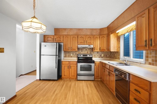 Kitchen featuring wood-finish flooring, ample wood cabinetry, light-toned countertops, and stainless steel appliances - 12311 25 Avenue Nw, Edmonton, AB 