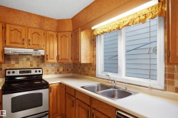 Wood cabinetry, tile backsplash, white countertops, stainless steel dual basin sink, and a double oven range - 