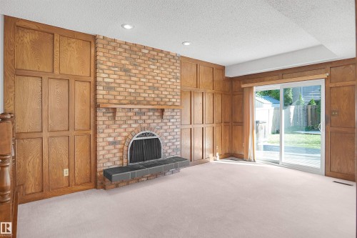 Brick fireplace with arched firebox and hearth, wood paneling, recessed lighting, and sliding glass door - 12311 25 Avenue Nw, Edmonton, AB 