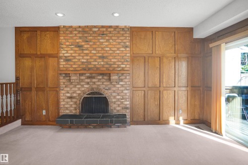 Brick fireplace with arched firebox and slate hearth, paneled wood accent walls, recessed lighting, and sliding glass door with exterior balcony - 12311 25 Avenue Nw, Edmonton, AB 