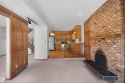 Brick fireplace with a black tile hearth, wood paneling, wood-finish flooring in the kitchen, and wood cabinetry - 