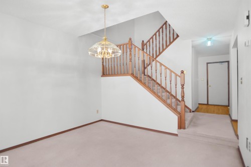 Open-concept space featuring a staircase with wood railings, a brass chandelier, and carpet flooring - 12311 25 Avenue Nw, Edmonton, AB 