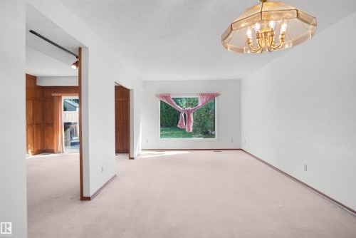 Open-concept living space with light-colored carpeting, white walls, and a large picture window - 12311 25 Avenue Nw, Edmonton, AB 
