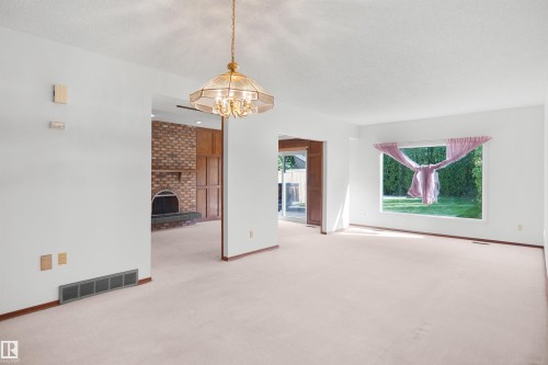 Recessed brick fireplace with a stone hearth, an overhead chandelier, and light-toned carpeting - 12311 25 Avenue Nw, Edmonton, AB 