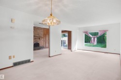 Recessed brick fireplace with a stone hearth, an overhead chandelier, and light-toned carpeting - 