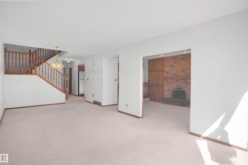 Open concept living space with staircase featuring wood balusters, and a brick-faced fireplace with hearth - 12311 25 Avenue Nw, Edmonton, AB 