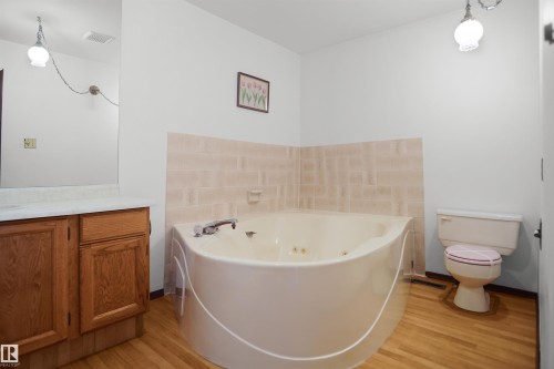 Jetted corner bathtub, wood-finish flooring, light wood vanity with laminate countertop, and wall-mounted light fixtures - 12311 25 Avenue Nw, Edmonton, AB 
