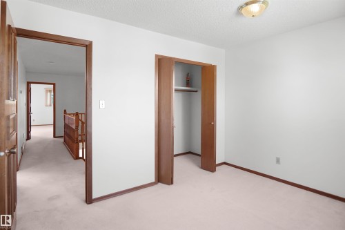 Carpeted flooring, white painted walls, wood-finish trim, and a built-in closet with shelving and hanging rod - 12311 25 Avenue Nw, Edmonton, AB 
