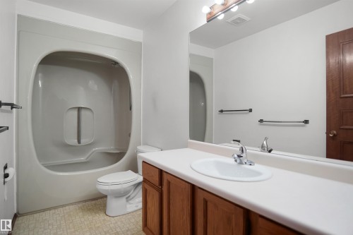 Integrated tub and shower combination, wood-finish vanity with an oval sink, chrome faucet, and a large wall-mounted mirror - 12311 25 Avenue Nw, Edmonton, AB 