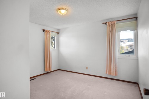 Neutral carpet flooring, two windows with drapery rods, a flush mount ceiling light, and white painted walls - 12311 25 Avenue Nw, Edmonton, AB 