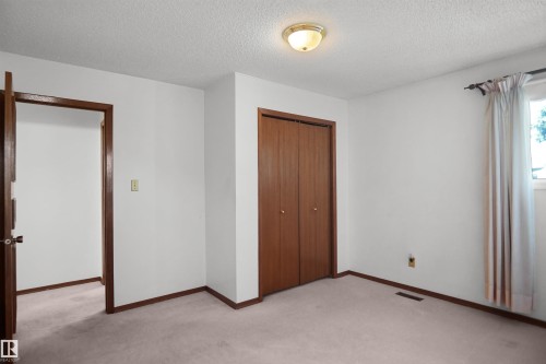 Light-colored carpeting, white painted walls, wood-finish bi-fold closet doors, and wood-finish trim - 12311 25 Avenue Nw, Edmonton, AB 