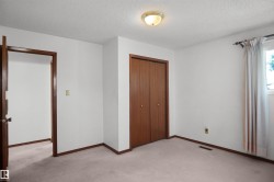 Light-colored carpeting, white painted walls, wood-finish bi-fold closet doors, and wood-finish trim - 