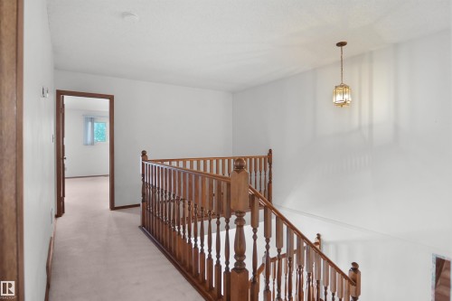 Wood-tone staircase with classic balusters, suspended ceiling fixture, and light-toned carpet flooring - 12311 25 Avenue Nw, Edmonton, AB 