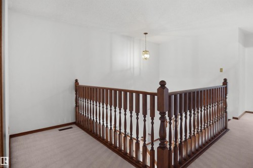 Hardwood railing with turned balusters, neutral carpet, and a decorative pendant light fixture - 12311 25 Avenue Nw, Edmonton, AB 