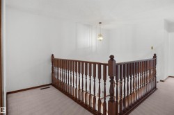 Hardwood railing with turned balusters, neutral carpet, and a decorative pendant light fixture - 