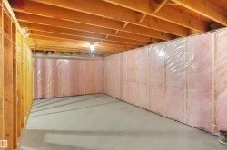 Unfinished basement featuring exposed wood joists, framed walls, insulation, and a concrete floor - 