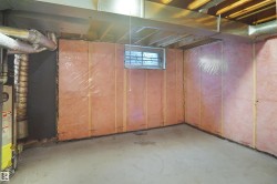 Unfinished lower level featuring exposed ceiling joists, concrete flooring, and a single window - 