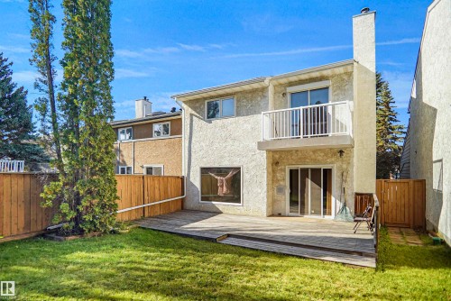 Expansive backyard featuring a manicured lawn, a full wooden fence, a multi-level wooden deck, and a second-story balcony with white railings - 12311 25 Avenue Nw, Edmonton, AB 