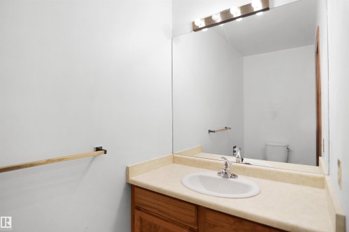 Vanity with an integrated sink, wood-finish cabinetry, and a full-width mirror - 12311 25 Avenue Nw, Edmonton, AB 