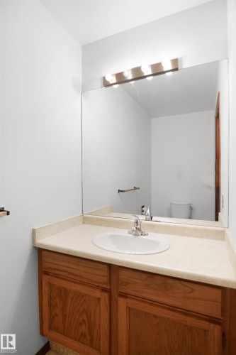 Vanity with wood-finish cabinetry, integrated sink, and light-toned countertop - 12311 25 Avenue Nw, Edmonton, AB 