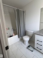 White tiled flooring, white bathtub, white vanity with drawer storage, and a built-in toilet - 