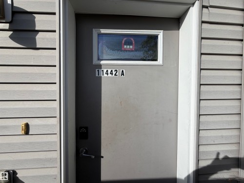 Grey exterior siding with a grey entry door featuring a transom window, modern door hardware, and a digital key pad - 11442 82 Street Nw, Edmonton, AB 