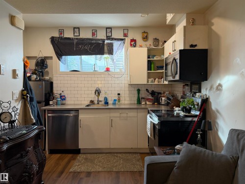 White subway tile backsplash, stainless steel dishwasher, white cabinetry, dark countertop, and wood-finish flooring - 11442 82 Street Nw, Edmonton, AB 