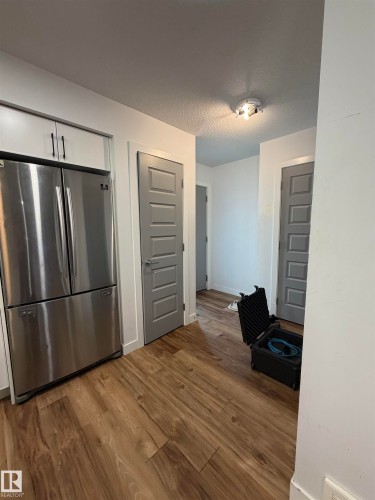 Stainless steel refrigerator, white cabinetry with dark hardware, wood-finish flooring, and panel-style interior doors - 11442 82 Street Nw, Edmonton, AB 
