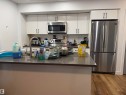 Stainless steel appliances, white cabinetry with black hardware, tile backsplash, wood-finish flooring, and a kitchen island with a built-in sink - 11442 82 Street Nw, Edmonton, AB 