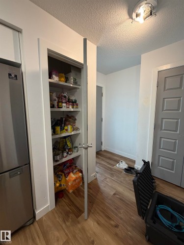 Built-in pantry with white shelving, stainless steel refrigerator, and wood-finish flooring - 11442 82 Street Nw, Edmonton, AB 