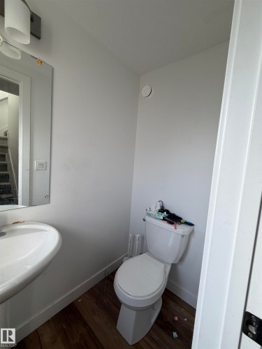 Pedestal sink with a wall-mounted mirror, white toilet, and wood-finish flooring - 11442 82 Street Nw, Edmonton, AB 