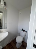 Pedestal sink with a wall-mounted mirror, white toilet, and wood-finish flooring - 