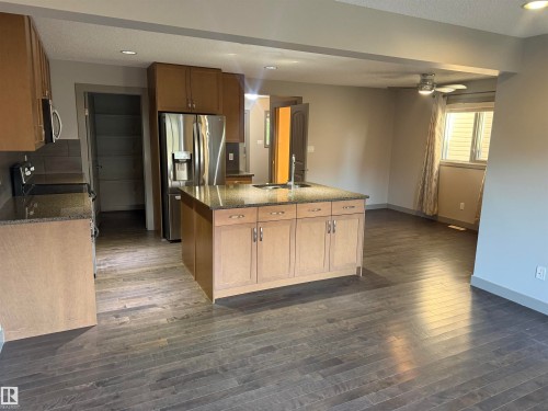 Kitchen featuring wood-finish cabinetry, granite countertops, and stainless steel appliances - 7065 Cardinal Way Sw, Edmonton, AB 